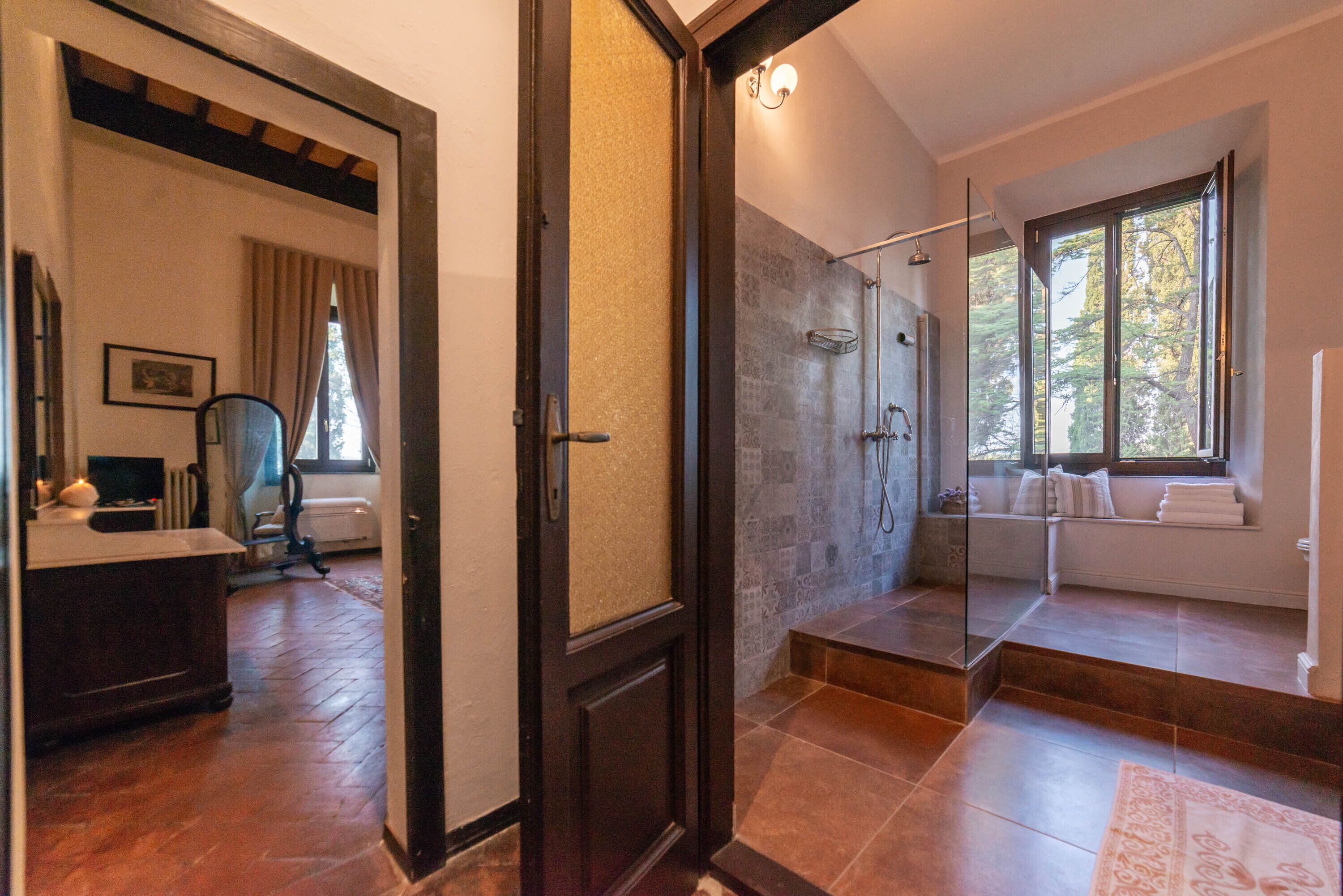 A modern bathroom with a glass shower enclosure, a built-in bench, and a view of the outdoors.