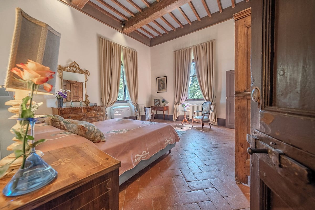 A bedroom with a bed, wooden furniture, a mirror, and a window with curtains.