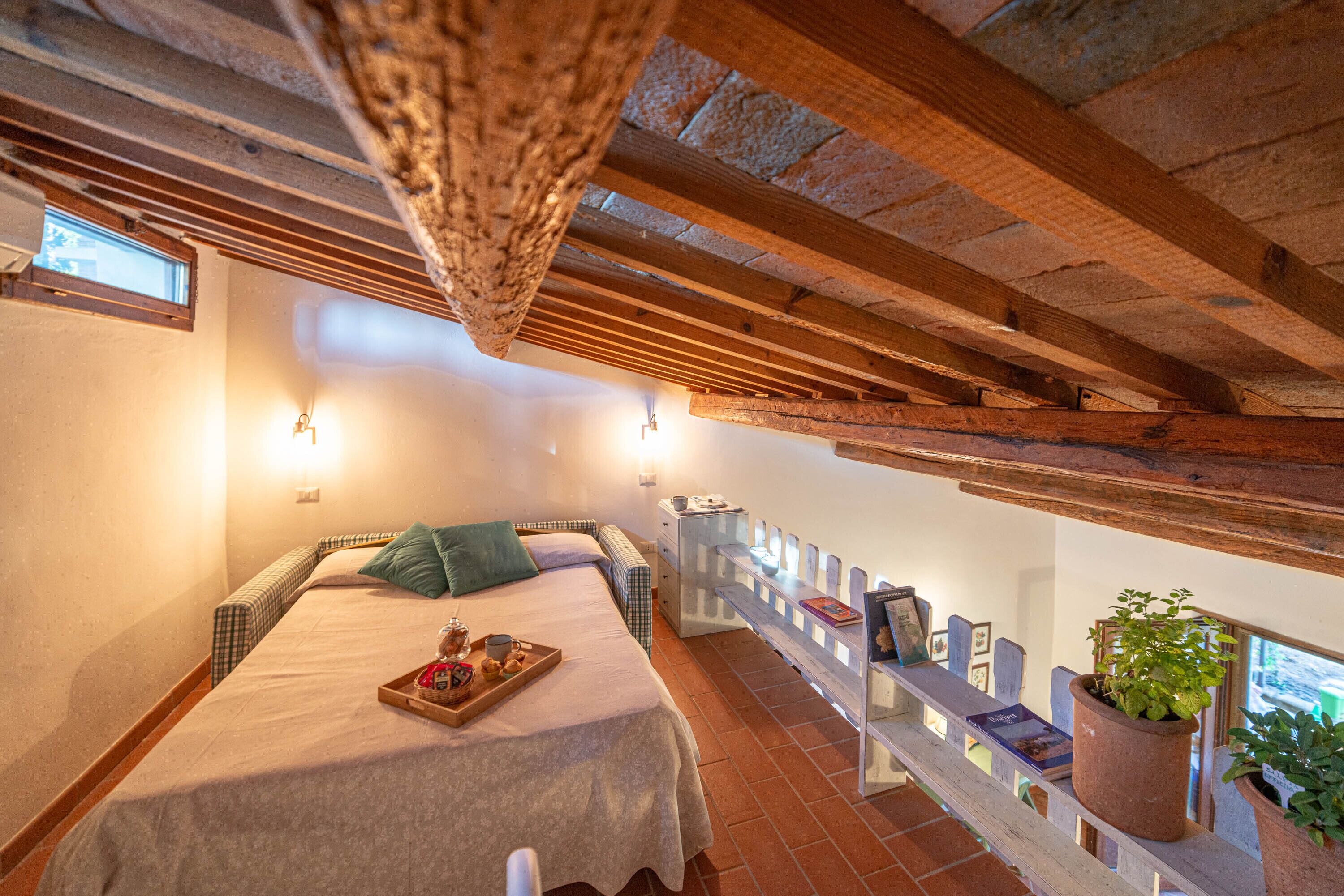 Ein gemütliches Schlafzimmer mit einem Bett, einer Kuchenschiene, einer Topfpflanze und Blick ins Freie.