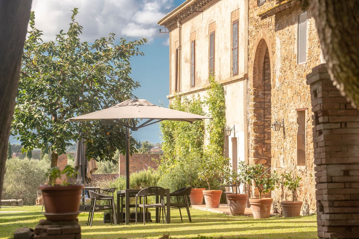 An outdoor patio area with a table and chairs, surrounded by potted plants and a large umbrella.