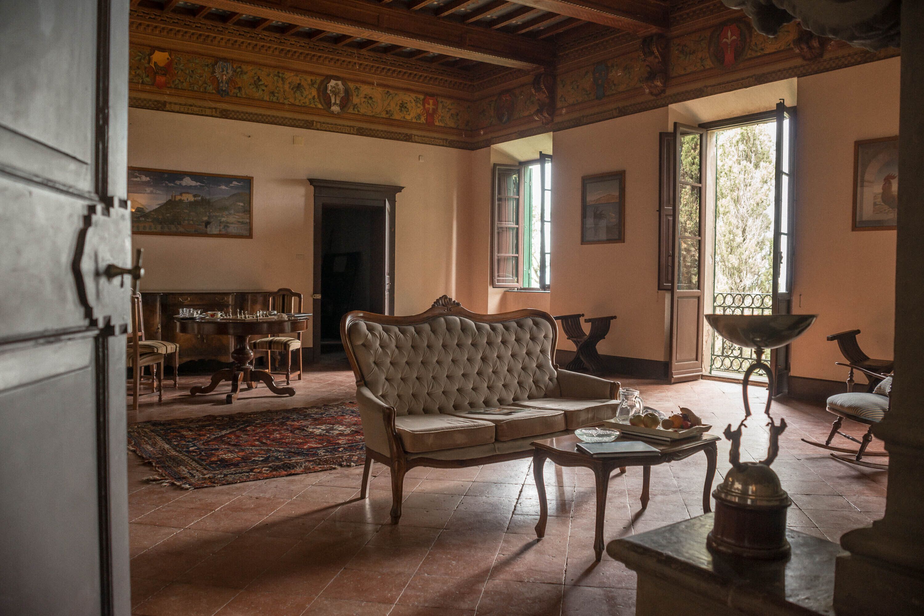 A room with a sofa, a table with a lamp, a painting on the wall, and a window with a view.
