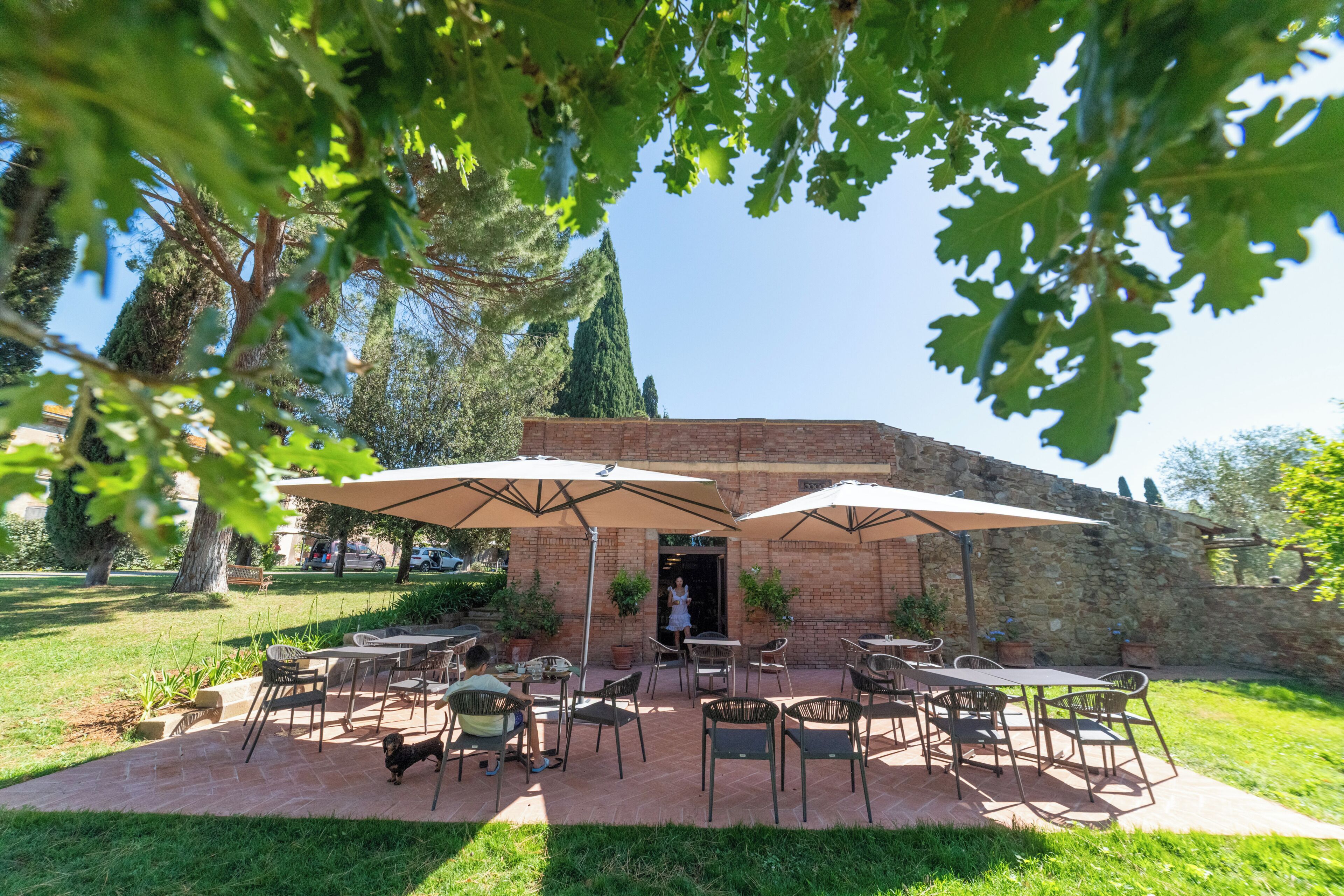 An outdoor patio with tables and chairs, surrounded by a brick wall and greenery.