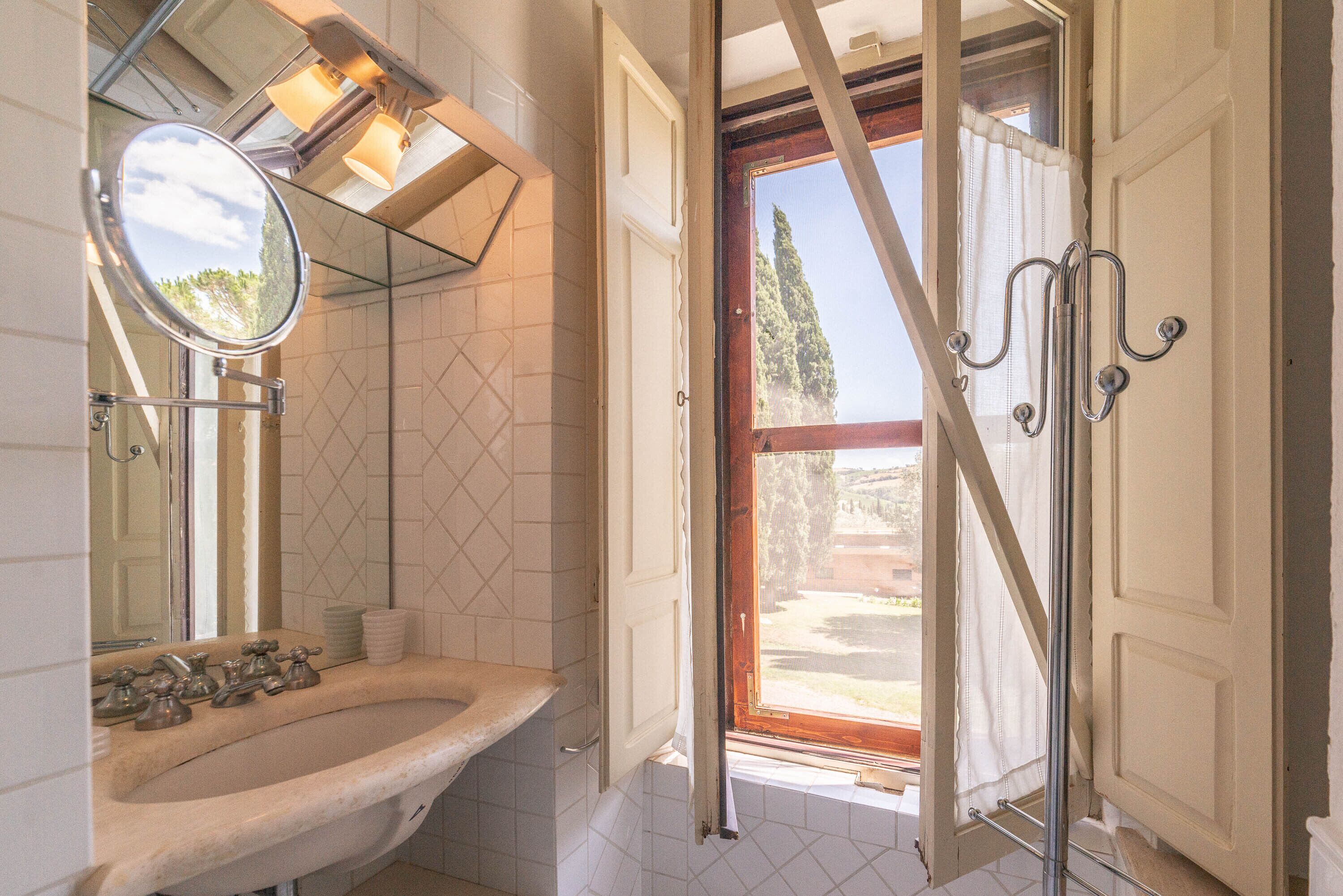 A bathroom with a sink, mirror, and window with curtains.