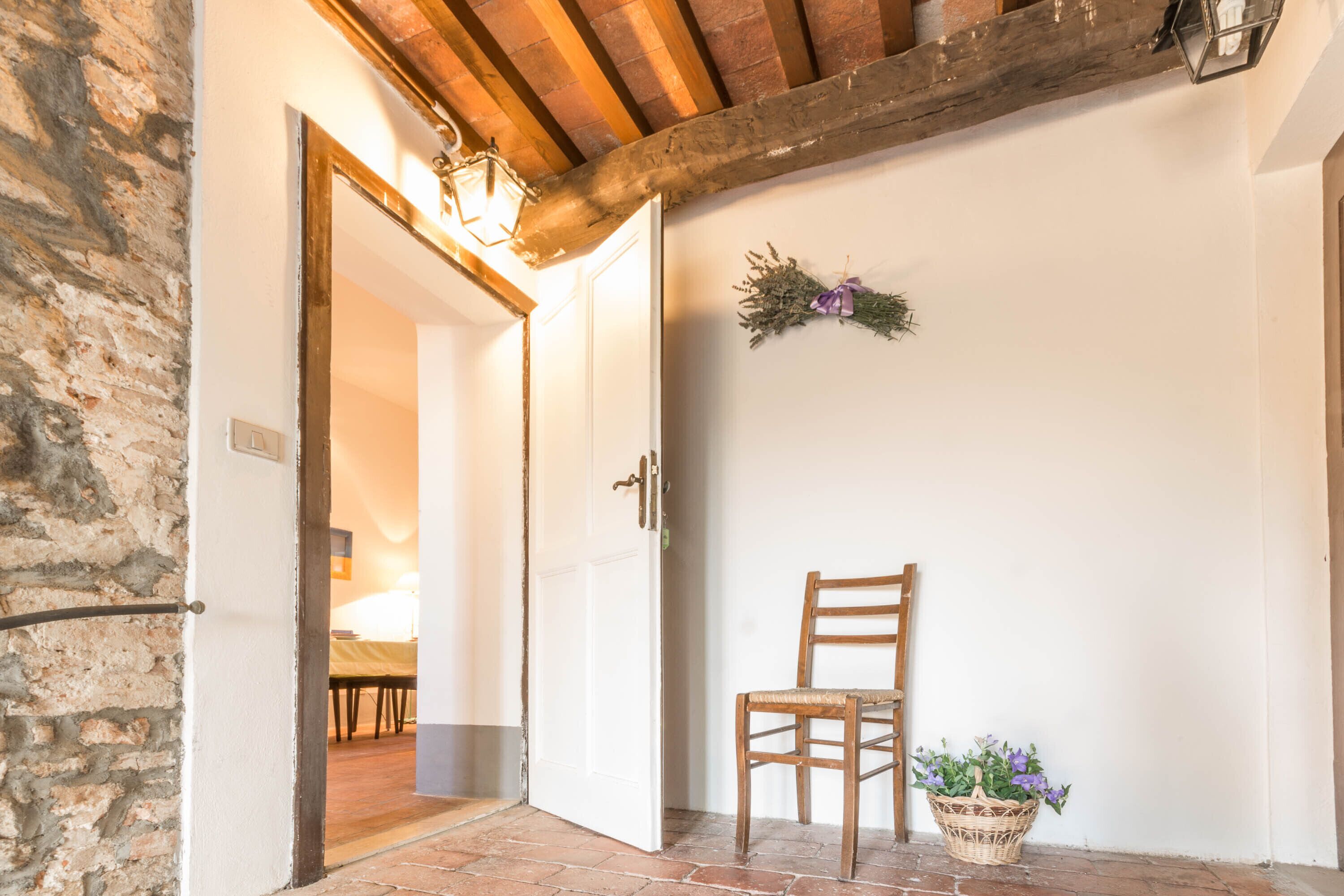 A rustic interior with a wooden chair, a wicker basket with flowers, and a door leading to another room.