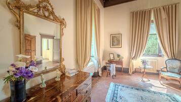 A room with a large ornate mirror, wooden dresser, and a small table with a vase of flowers.