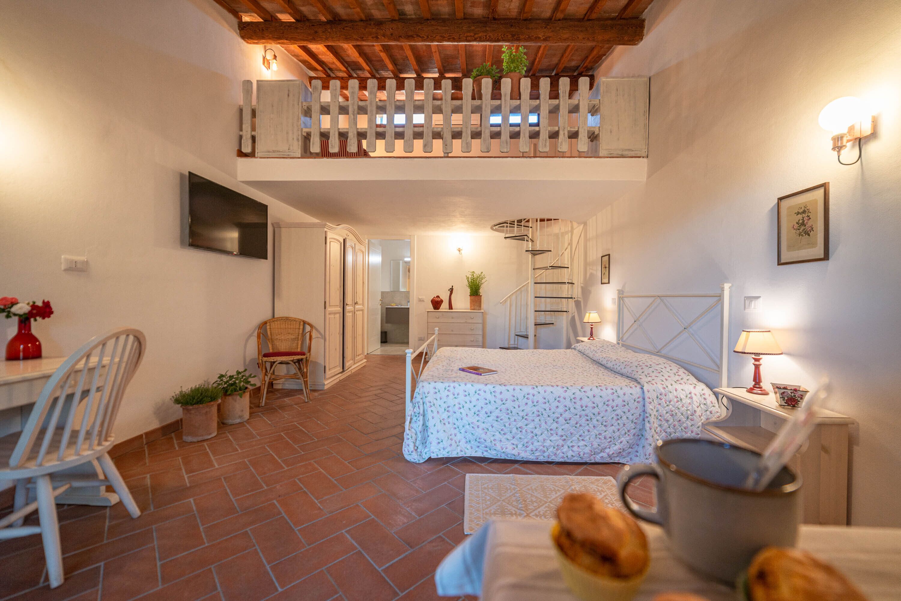A cozy bedroom with a bed, a desk, and a chair. There is a staircase leading to an upper level.