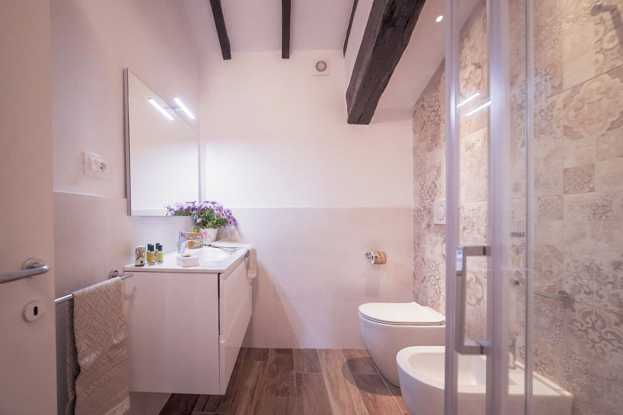 A modern bathroom with a white vanity, a glass shower enclosure, and a patterned wall.