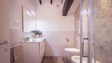 A modern bathroom with a white vanity, a glass shower enclosure, and a patterned wall.