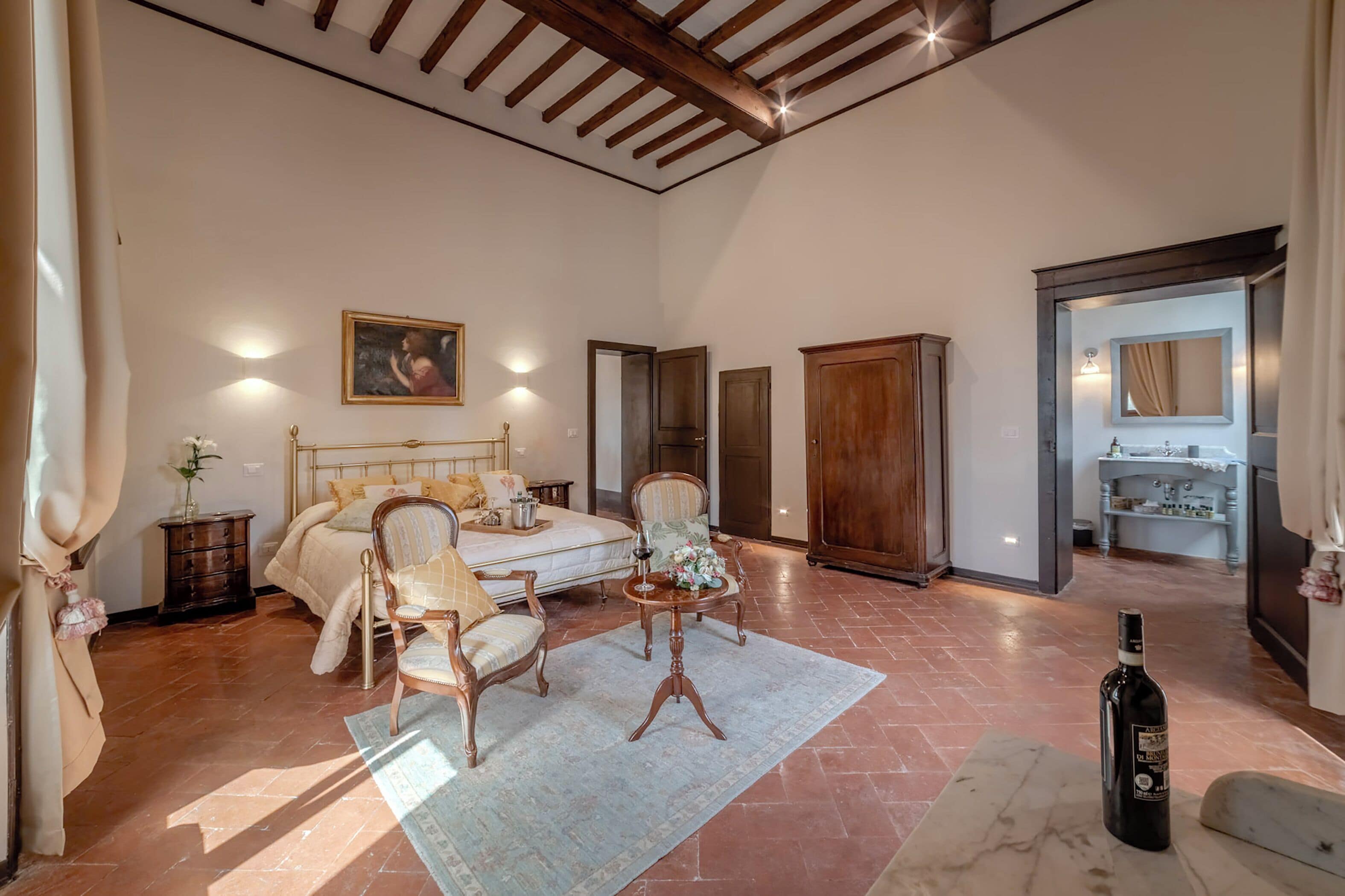 A spacious bedroom with a large bed, two chairs, a small table, and a wardrobe.