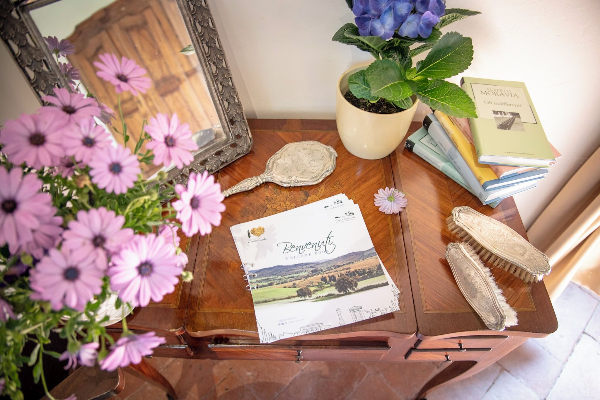 A wooden table with a welcome booklet, a mirror, a potted plant, and books.