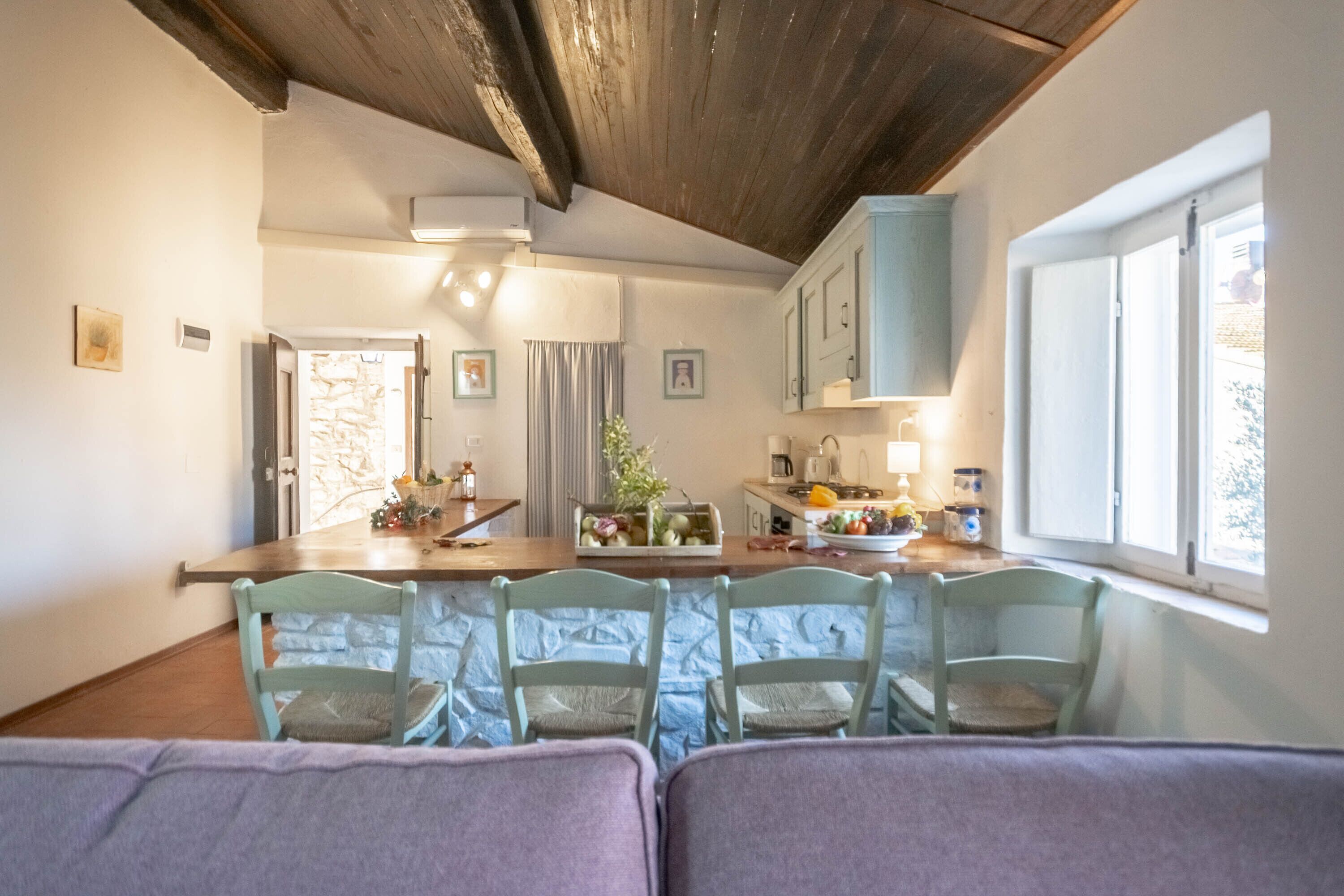 A cozy kitchen with a wooden ceiling, a dining area with four chairs, and a window with natural light.