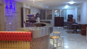 A modern kitchen with a built-in island, bar stools, and a seating area with a red cushioned bench. - Hotel Riposo (Gatteo)