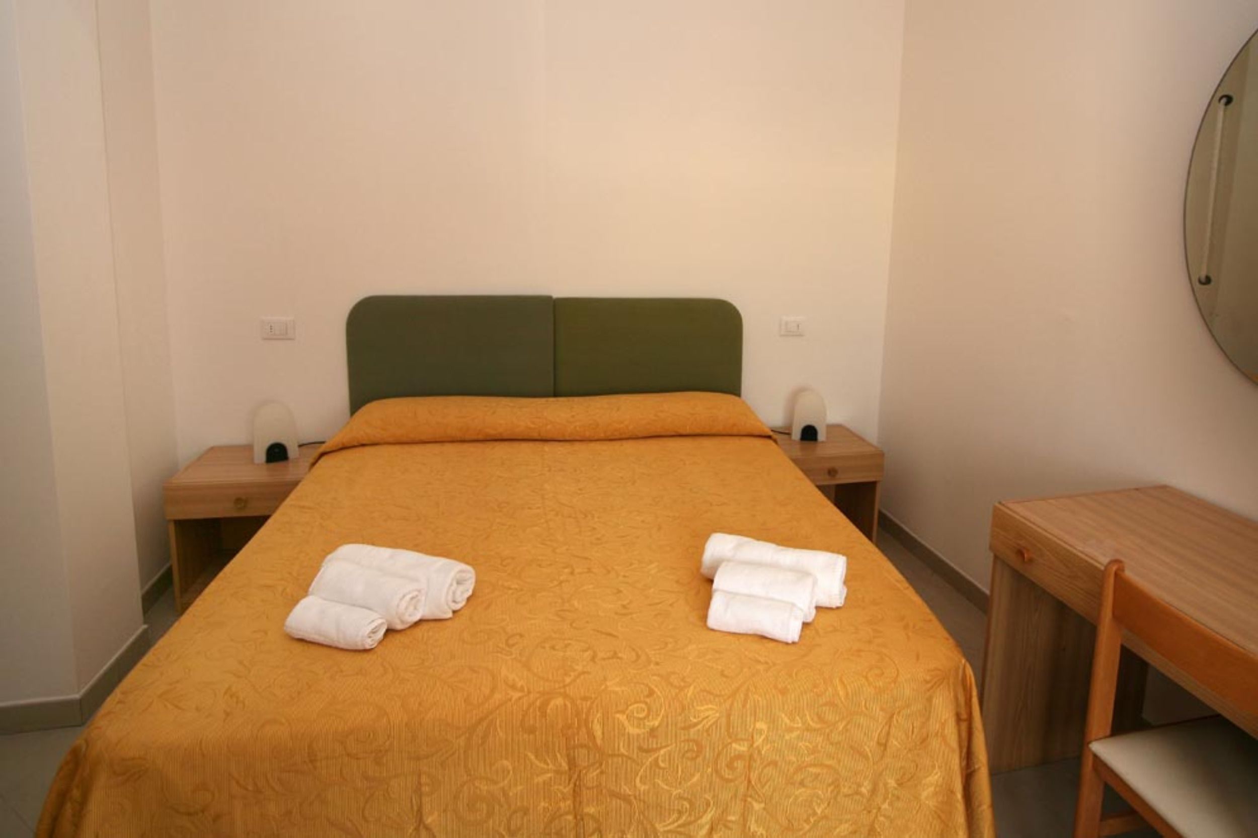 A single bed with an orange bedspread, two nightstands, and a wooden bench.