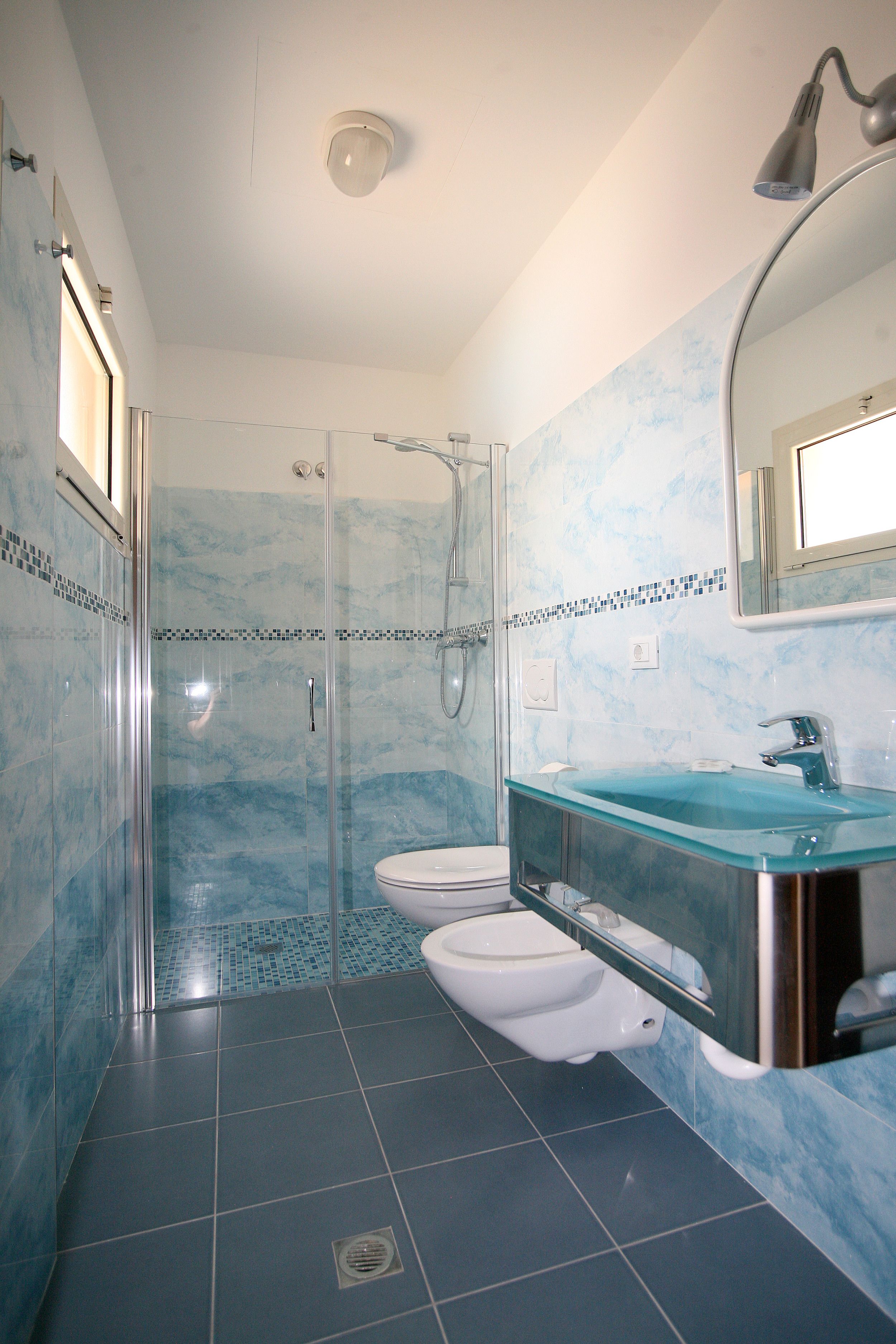 A bathroom with a glass-enclosed shower, a white toilet, and a glass sink with a chrome faucet.