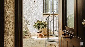An open door revealing a tiled patio with a potted plant, a metal staircase, and a barred window.