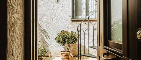 An open door revealing a tiled patio with a potted plant, a metal staircase, and a barred window.