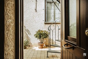 An open door revealing a tiled patio with a potted plant, a metal staircase, and a barred window.