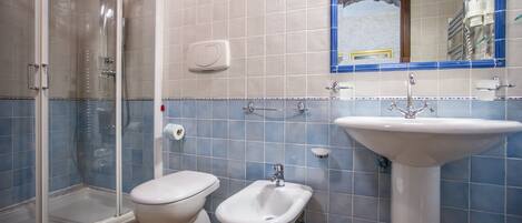 A bathroom with a shower, toilet, bidet, and sink.