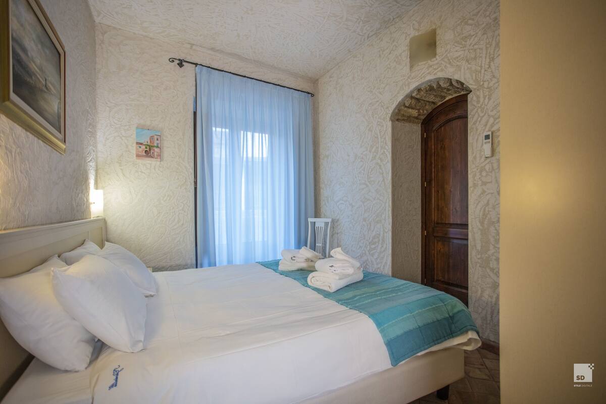 A neatly made bed with white linens and a blue-striped bedspread, a wooden door, and a framed picture on the wall.