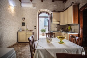 A dining area with a table set for two, a kitchen with wooden cabinets, and a doorway leading outside.
