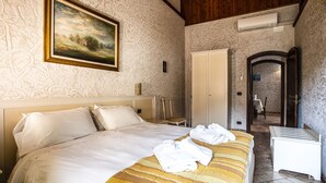 A hotel room with a large bed, a painting on the wall, a wardrobe, and a bathroom visible through an open door.