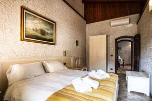 A hotel room with a large bed, a painting on the wall, a wardrobe, and a bathroom visible through an open door.
