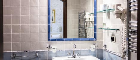 Une salle de bain avec un lavabo blanc, des murs recouverts de carreaux bleus et blancs, un miroir avec un cadre bleu et un porte-serviettes sur lequel est posée une serviette et un sèche-cheveux.