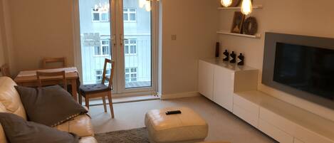 Un salon comprenant un canapé, un téléviseur et un coin repas avec une table et des chaises.