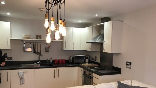 A modern kitchen with white cabinets, a black countertop, and a built-in microwave. There is a white sofa with gray cushions in the living area. - Mermaid Bay (Cardiff)