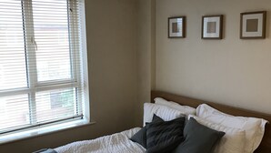 A bedroom with a bed, a window with blinds, and a ceiling light. - Mermaid Bay (Cardiff)