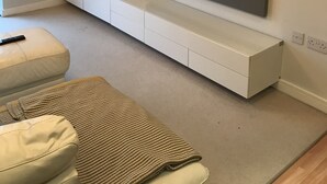 A modern living room with a flat-screen TV mounted on a white entertainment unit, a beige sofa, and a patterned rug. - Mermaid Bay (Cardiff)