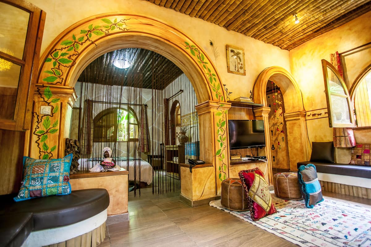 A room with wooden arches, a bed with a view through a window, a small table, and a decorative pillow.