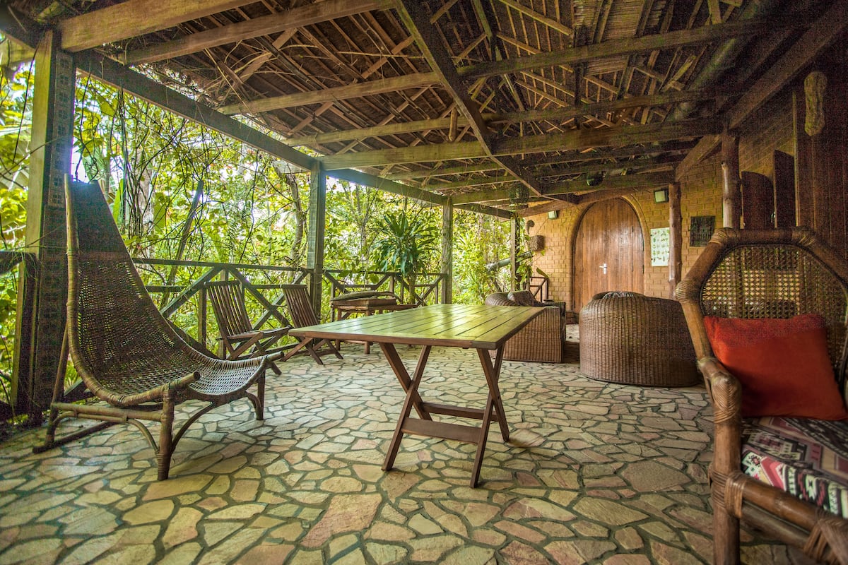 An outdoor patio with stone flooring, wooden furniture, and a thatched roof structure.