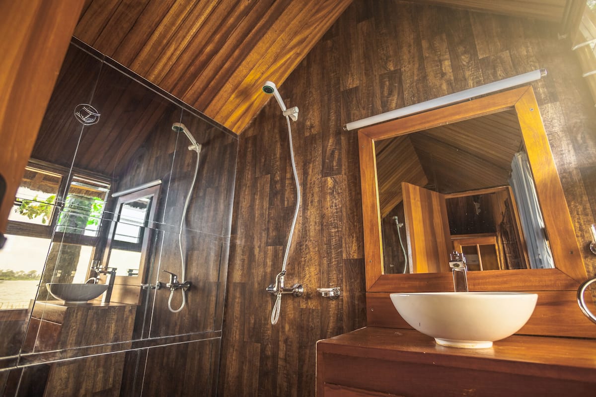 A wooden bathroom with a large mirror, a white sink, and a shower.