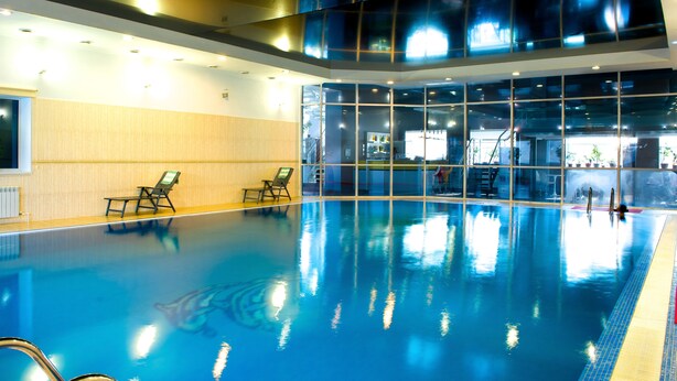 Une piscine intérieure à l’eau claire, dotée de deux chaises longues et d’un mur en verre.