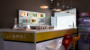Un espace bar avec un comptoir où sont exposées différentes boissons, un réfrigérateur rempli de boissons et un coin salon avec des chaises.