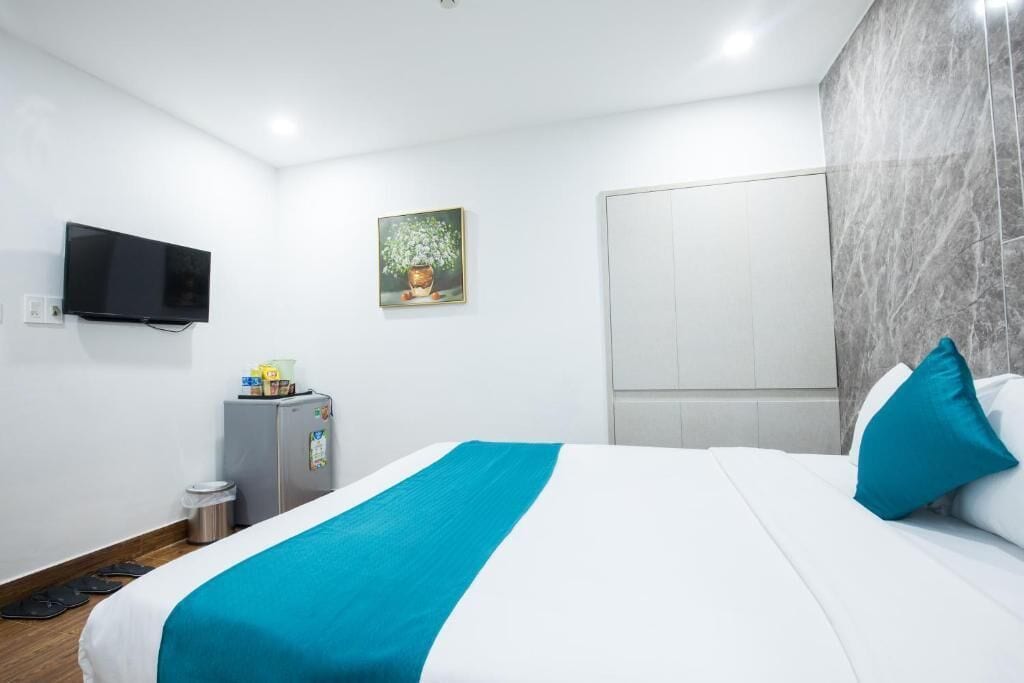 A hotel room with a bed, a television mounted on the wall, a small refrigerator, and a painting on the wall.