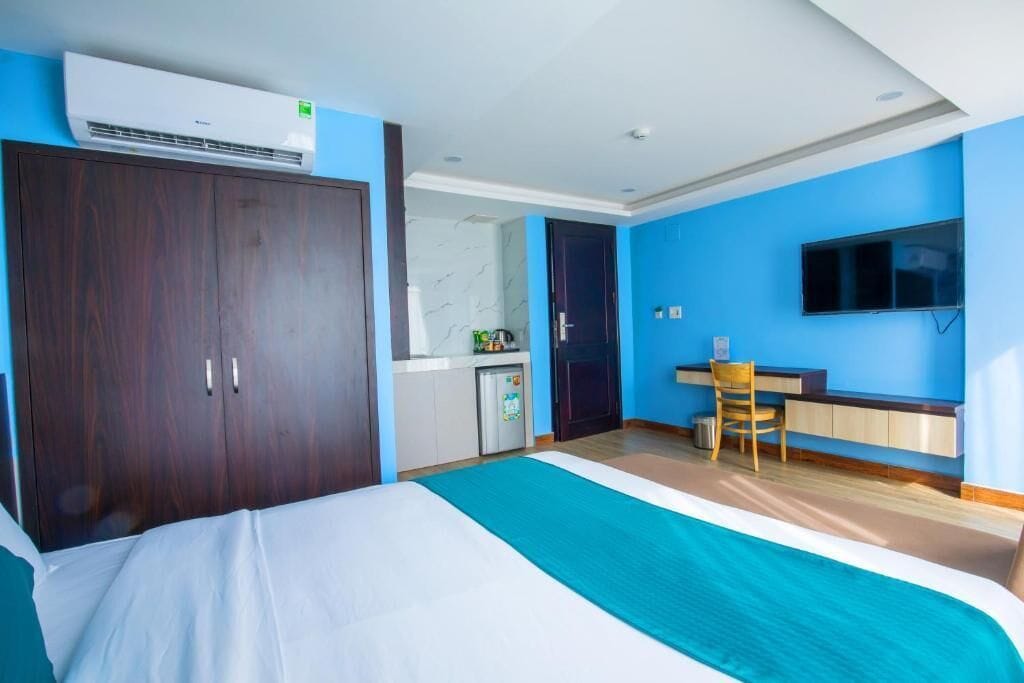 Habitación de hotel con cama, escritorio, silla, televisor montado en la pared y aire acondicionado.
