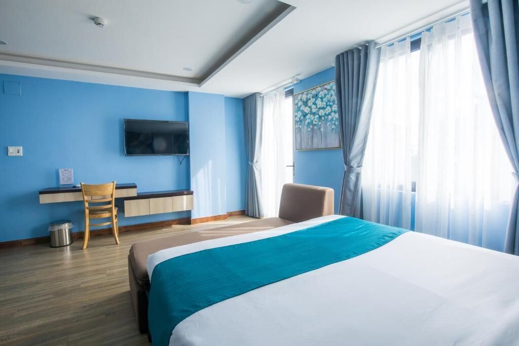 A hotel room with a bed, a desk, a chair, a TV, and a window with curtains.
