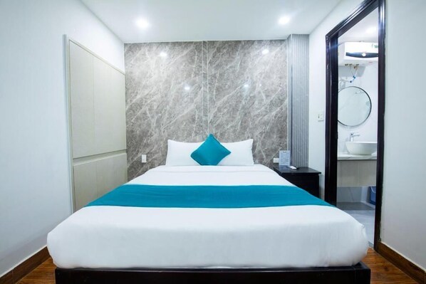 A modern hotel room with a large bed, marble wall, and a bathroom visible through an open door. - Blue Ocean Beachside Hotel Danang (Da Nang)