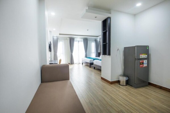 A hotel room with a bed, a sofa, a refrigerator, and a trash bin. - Blue Ocean Beachside Hotel Danang (Da Nang)