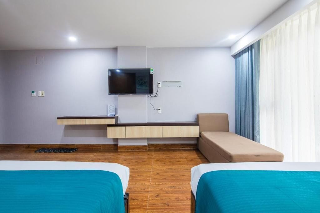 A hotel room with two beds, a TV mounted on the wall, a small sofa, and a window with curtains.