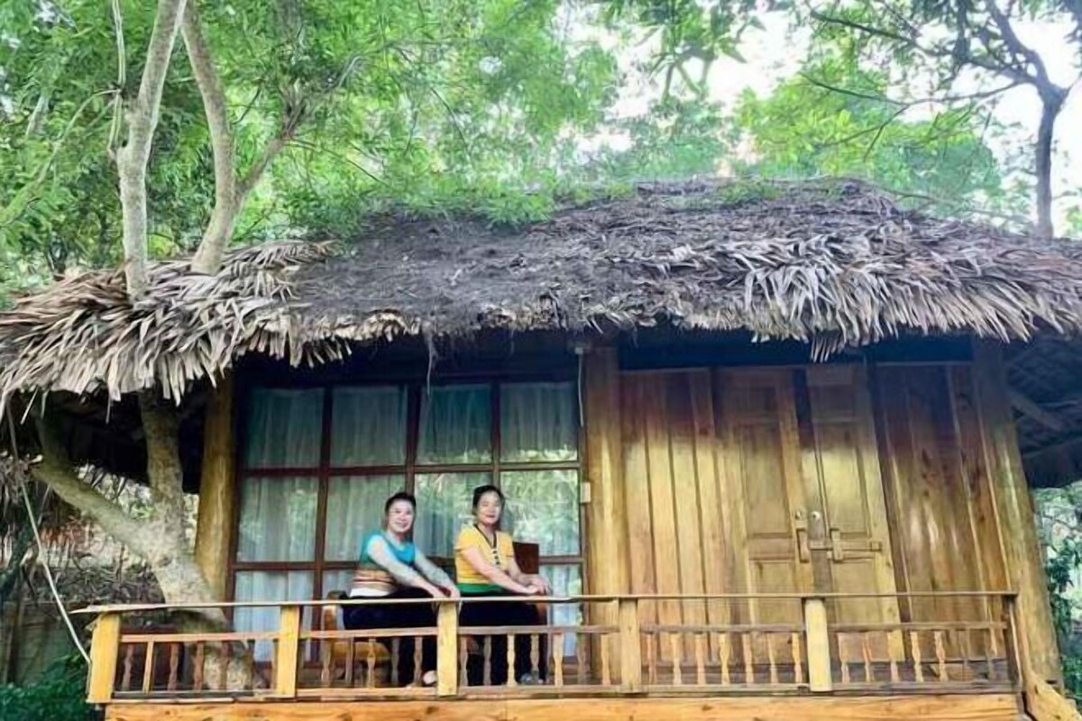 Una cabaña de madera con techo de paja, un balcón y una ventana con vistas al bosque.