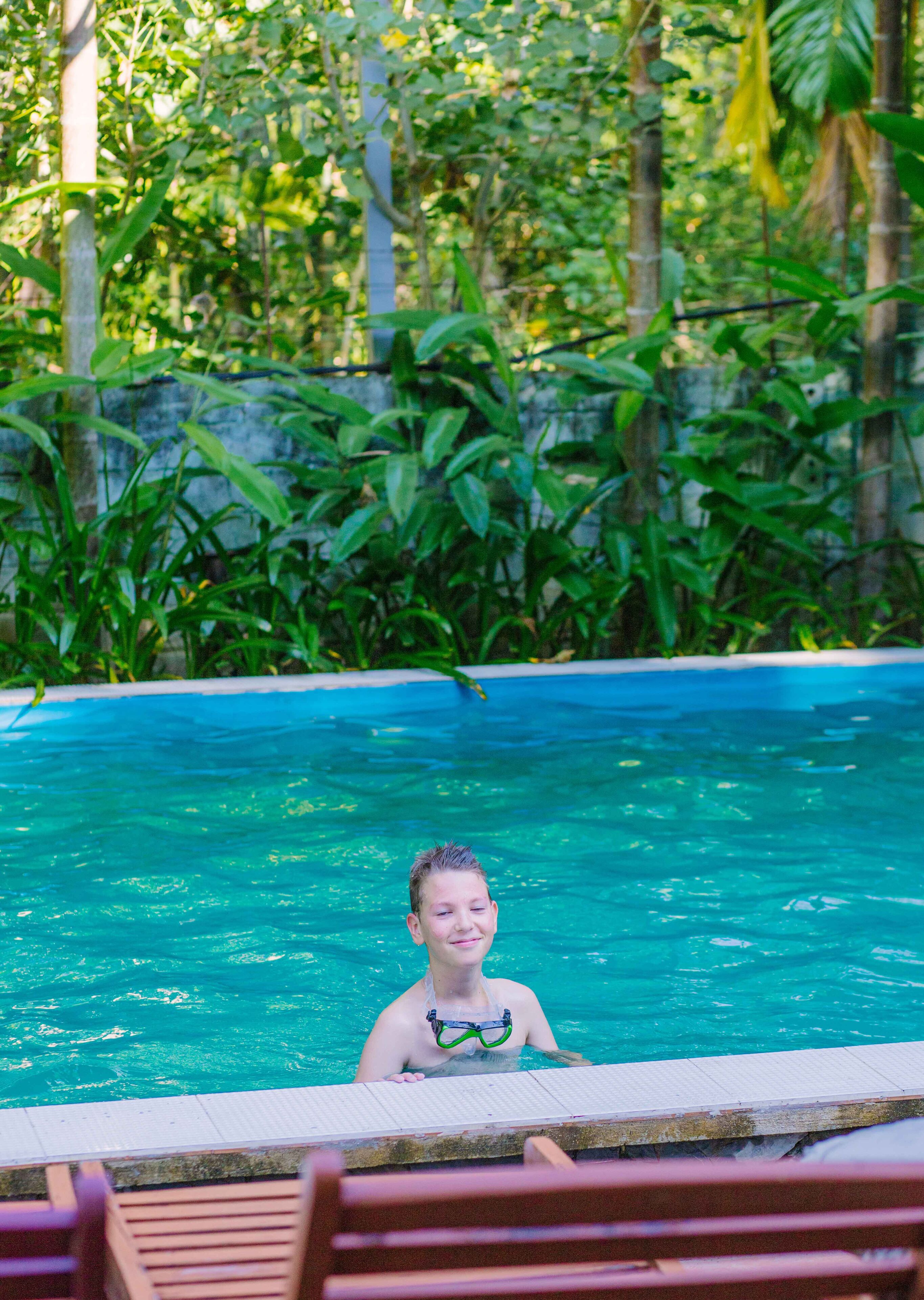 Une personne se trouve dans une piscine, avec une vue dégagée sur le bord de la piscine et la végétation environnante.
