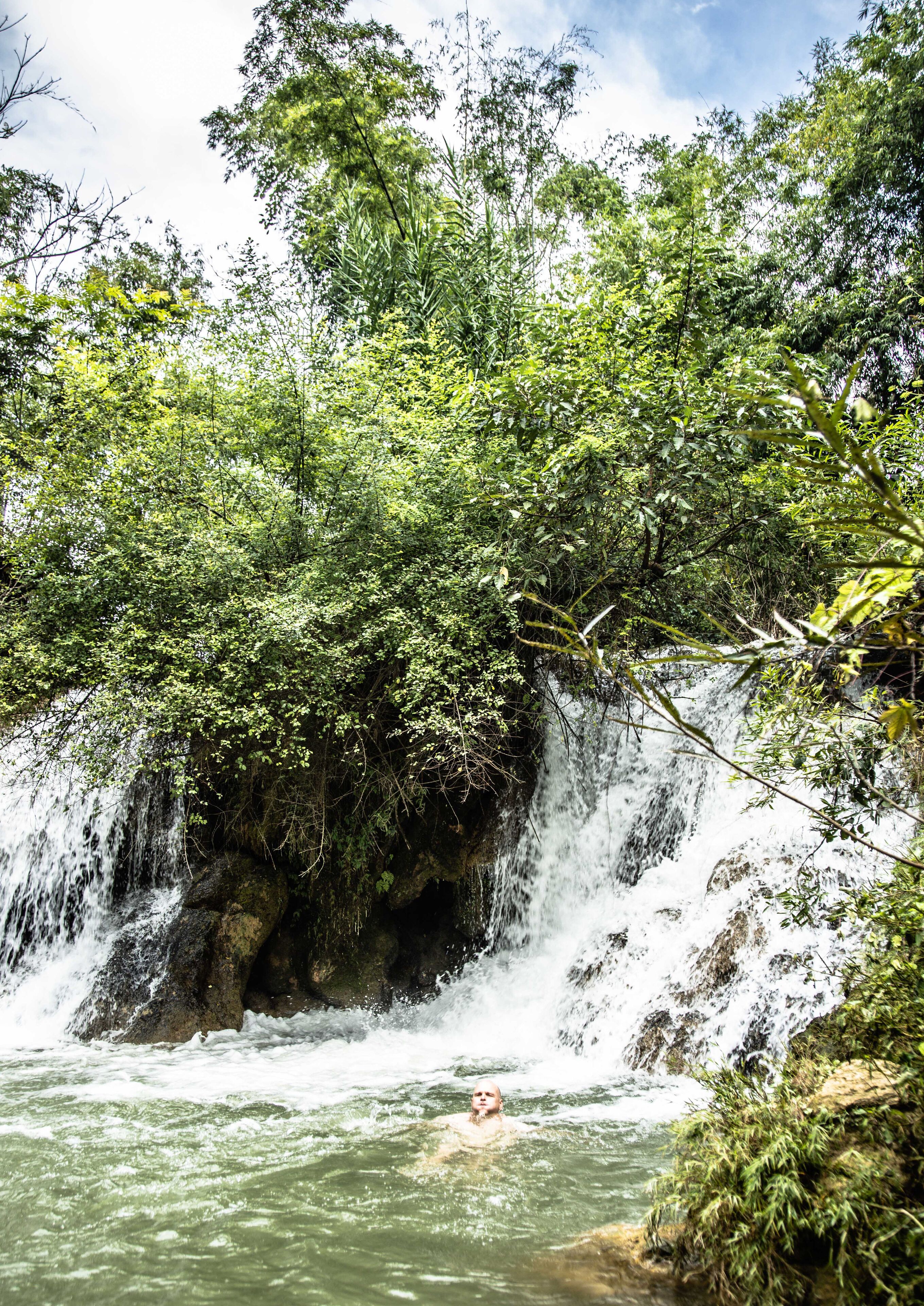 Une cascade dans une zone boisée, avec une personne qui nage dans l’eau.
