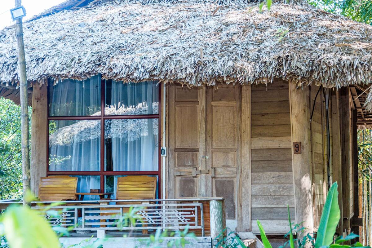 Een landelijk houten huis met rieten dak, grote ramen en een houten deur.