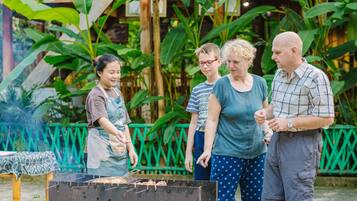 Un groupe de personnes rassemblées autour d’un barbecue dans un cadre extérieur, entouré d’une végétation luxuriante.
