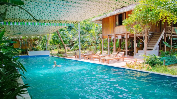Un área de piscina con sillas de descanso y una persona nadando.