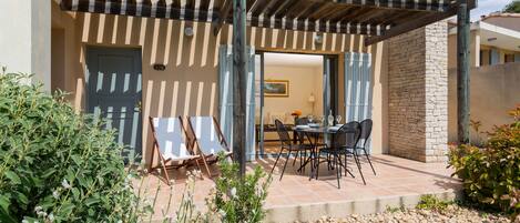 A covered patio area with a stone wall, outdoor seating, and a door leading to an interior space.