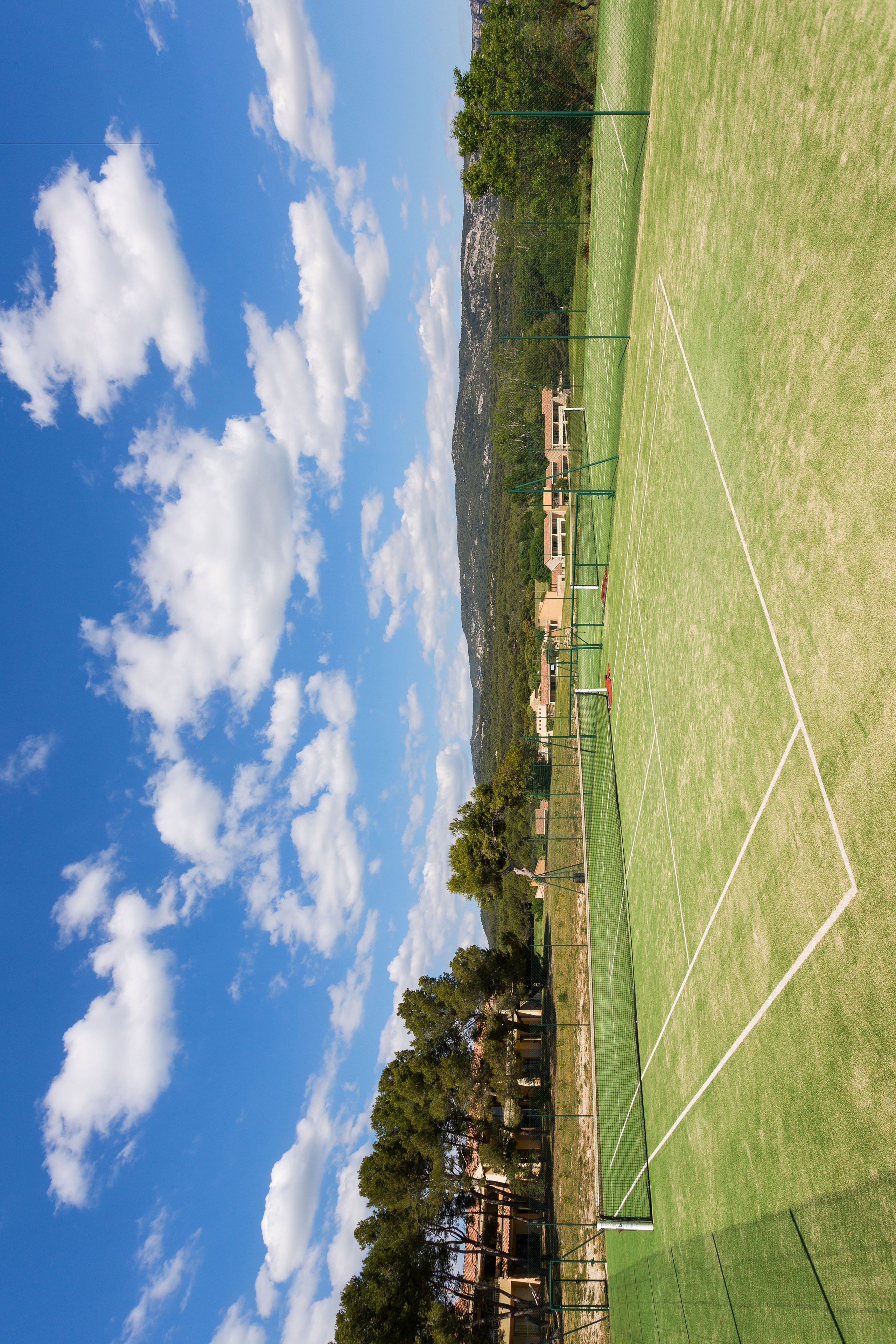 Un court de tennis avec un filet, entouré d’arbres et de bâtiments.